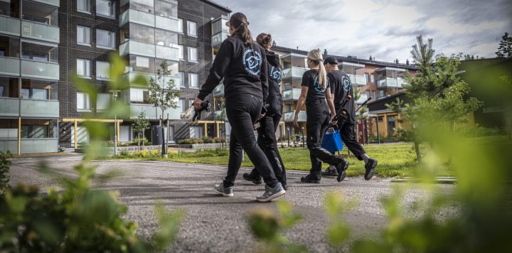 Fire renholdere går mot en moderne boligblokk for å utføre renholdsoppgaver.