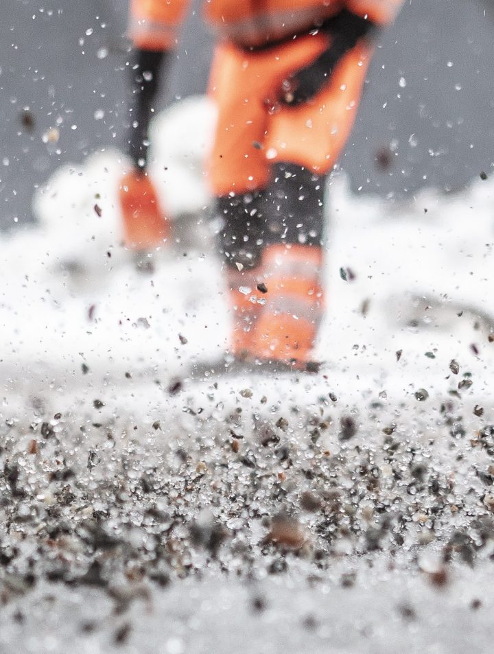 En av våre ansatte sprer strøgrus utover bakken i en bygård for å sikre trygg ferdsel på eiendommen.